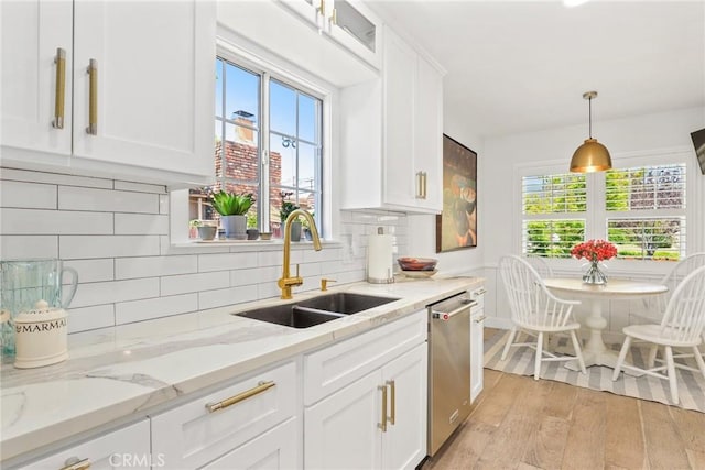 kitchen featuring light wood-style floors, stainless steel dishwasher, white cabinets, a sink, and hanging light fixtures