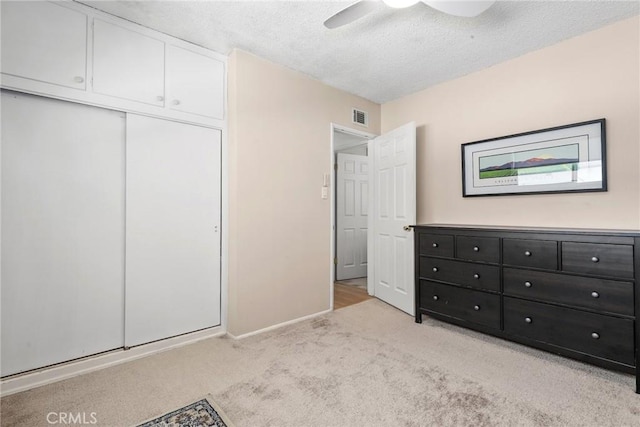 unfurnished bedroom with a textured ceiling, a closet, light colored carpet, visible vents, and baseboards