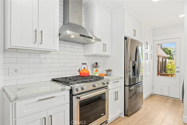 kitchen with tasteful backsplash, white cabinets, wall chimney range hood, light wood-type flooring, and stainless steel appliances