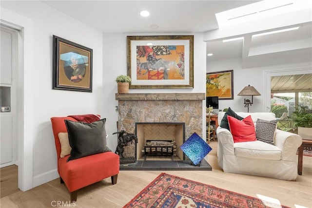 sitting room with a stone fireplace, recessed lighting, wood finished floors, and baseboards