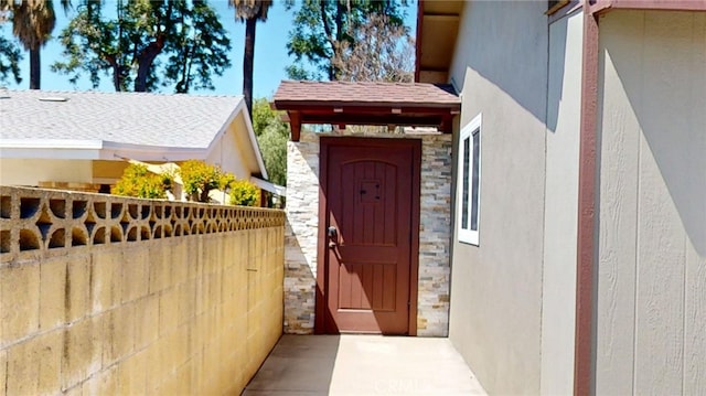 doorway to property with fence, stone siding, and stucco siding