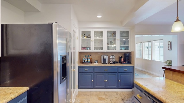 kitchen with glass insert cabinets, blue cabinetry, stainless steel fridge, decorative light fixtures, and backsplash