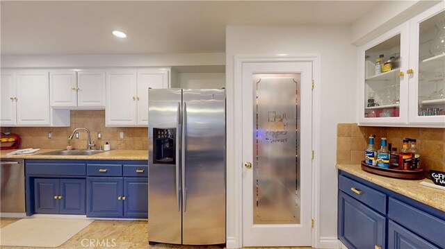 kitchen with tasteful backsplash, blue cabinets, white cabinets, appliances with stainless steel finishes, and a sink