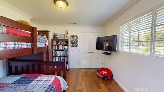 bedroom with visible vents, baseboards, a closet, crown molding, and wood finished floors