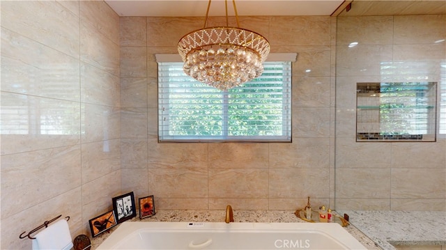 full bath featuring tile walls, an inviting chandelier, and a garden tub