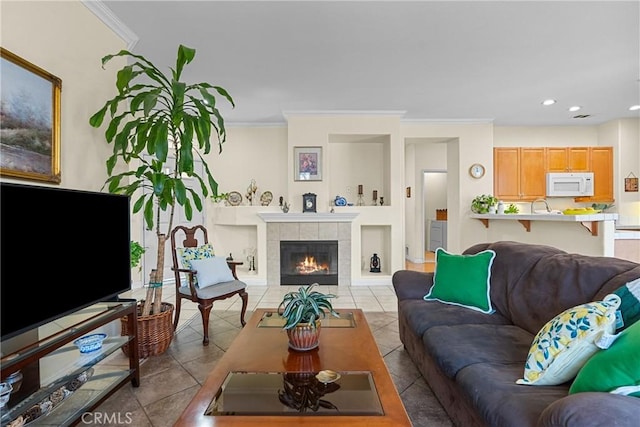 living room with a tiled fireplace, ornamental molding, and light tile patterned flooring