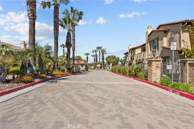 view of road featuring traffic signs, a gated entry, a residential view, curbs, and a gate