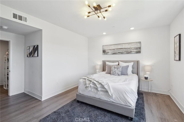 bedroom with an inviting chandelier, wood finished floors, visible vents, and baseboards