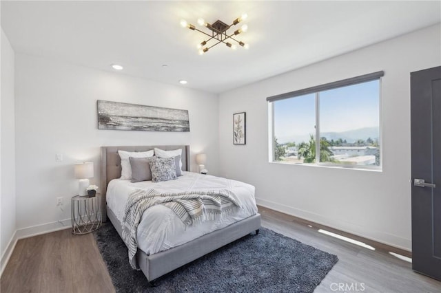 bedroom featuring baseboards, recessed lighting, wood finished floors, and a notable chandelier