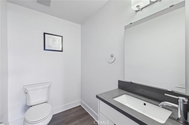 bathroom featuring wood finished floors, toilet, vanity, baseboards, and visible vents