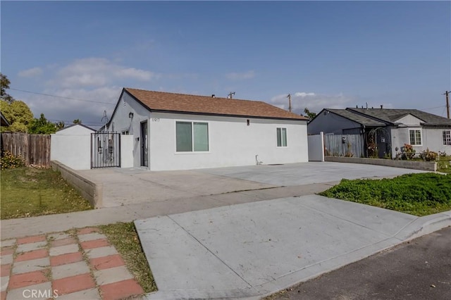 rear view of property with driveway, fence, stucco siding, and a gate