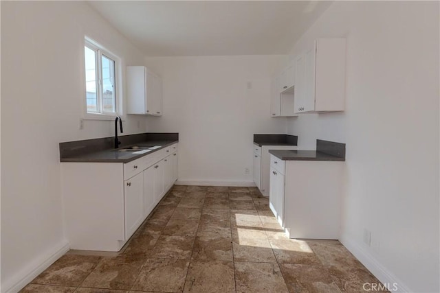 kitchen with white cabinets, baseboards, a sink, and dark countertops