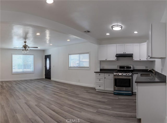 kitchen with a sink, stainless steel gas range, dark countertops, and under cabinet range hood