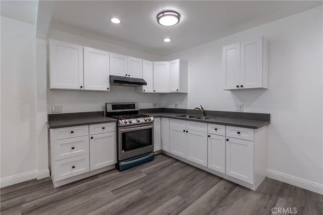 kitchen with a sink, stainless steel gas range, dark countertops, and under cabinet range hood