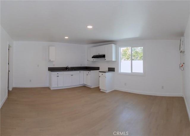 kitchen with light wood-type flooring, white cabinets, under cabinet range hood, dark countertops, and baseboards