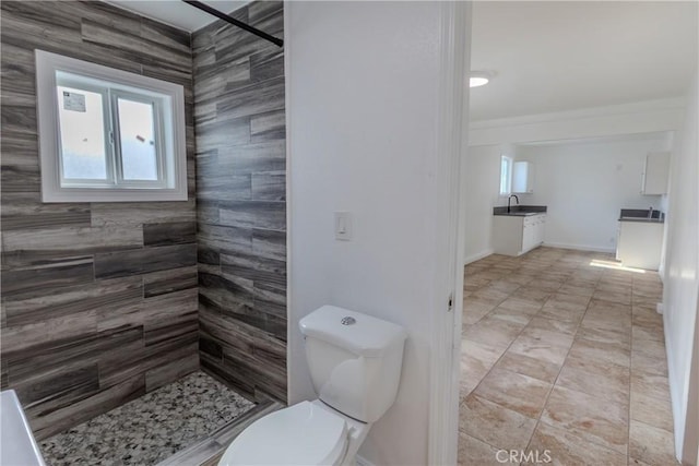 bathroom with tiled shower, tile patterned flooring, toilet, a sink, and baseboards