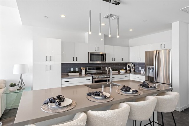 kitchen with decorative backsplash, a kitchen breakfast bar, white cabinets, a sink, and appliances with stainless steel finishes