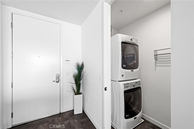 laundry room featuring baseboards, laundry area, dark wood finished floors, and stacked washer / dryer