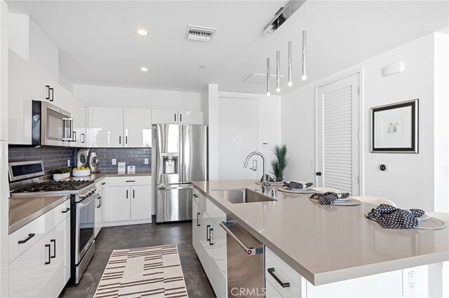 kitchen with backsplash, appliances with stainless steel finishes, a sink, white cabinetry, and an island with sink
