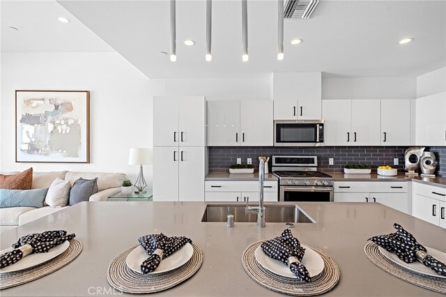 kitchen featuring white cabinets, a sink, stainless steel appliances, tasteful backsplash, and visible vents