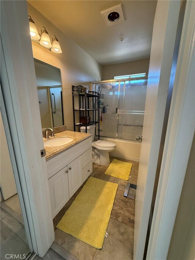 full bath with toilet, vanity, and bath / shower combo with glass door