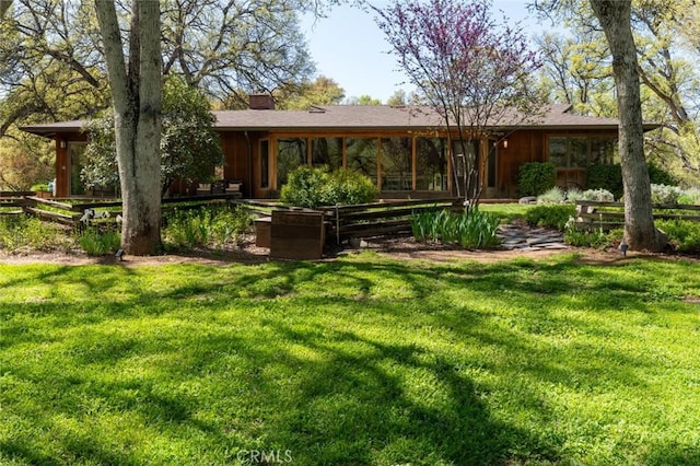 rear view of house with a lawn, fence, and a chimney
