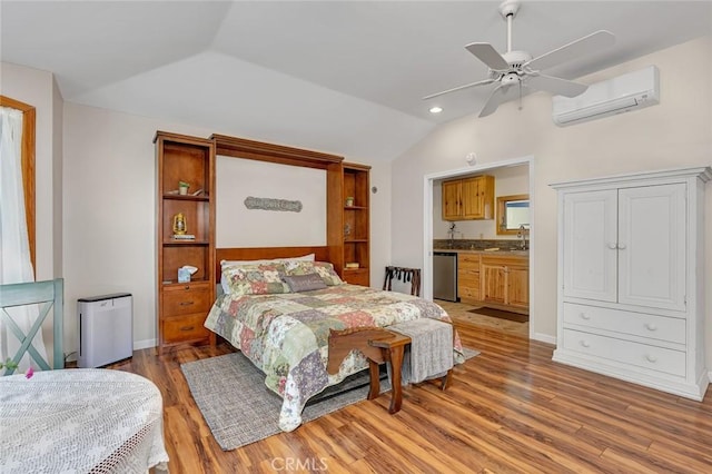 bedroom with lofted ceiling, connected bathroom, a wall mounted AC, a sink, and light wood finished floors