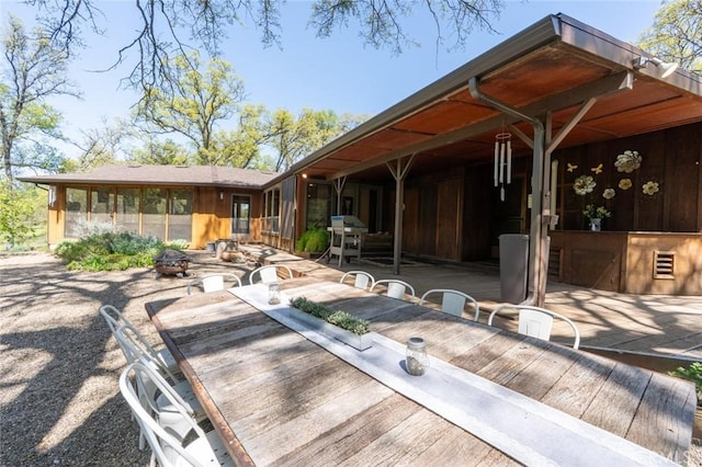 view of patio featuring outdoor dining area, a fire pit, a sunroom, and area for grilling