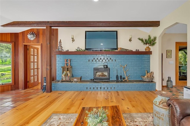 living area featuring arched walkways, a healthy amount of sunlight, beam ceiling, and wood finished floors