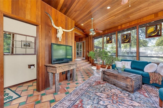 living area featuring wooden walls, wood ceiling, baseboards, and a ceiling fan