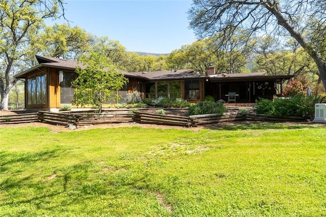rear view of property featuring a sunroom, a lawn, and a chimney