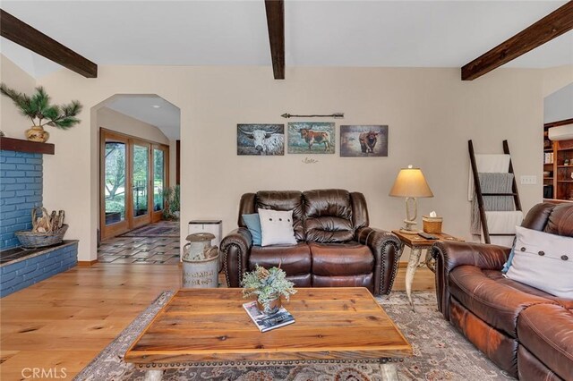 living area with wood finished floors, arched walkways, and beam ceiling