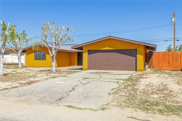 view of front facade with driveway, a garage, stucco siding, and fence