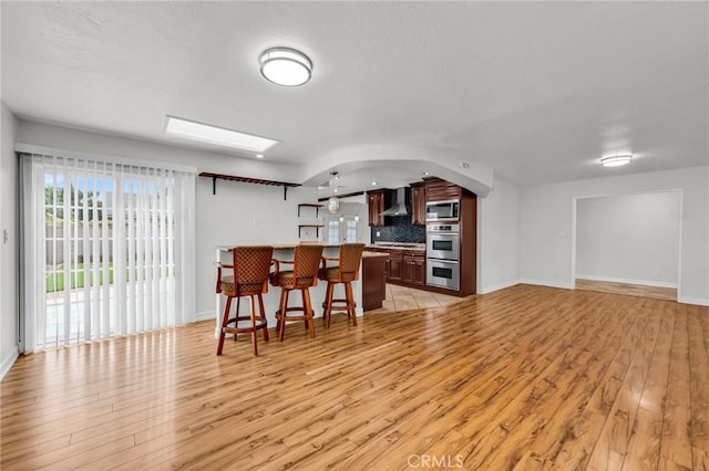 12195 Monte Vista Ave, Chino, CA 91710 - kitchen with a breakfast bar, wall chimney exhaust hood, decorative backsplash, stainless steel appliances, and light wood finished floors