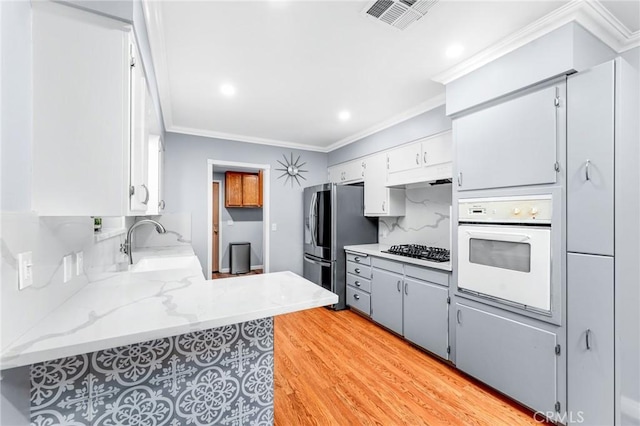 kitchen featuring white oven, visible vents, a sink, ornamental molding, and gas cooktop