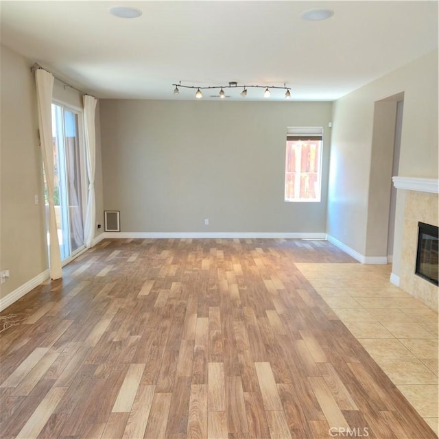 24963 Sunset Vista Ave, Menifee, CA 92584 - unfurnished living room featuring light wood-style flooring, a tile fireplace, healthy amount of natural light, and baseboards