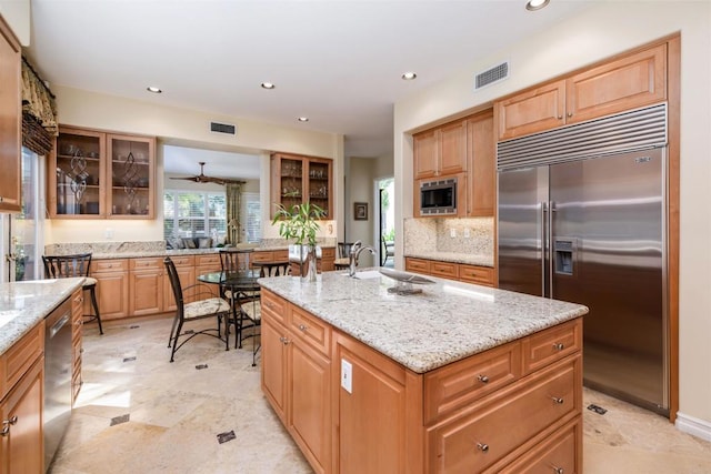 kitchen featuring glass insert cabinets, built in appliances, visible vents, and a center island with sink