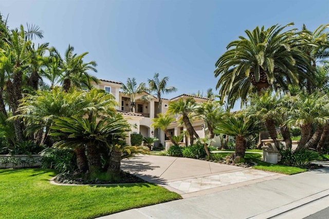 mediterranean / spanish home featuring a tile roof, a front lawn, driveway, and stucco siding