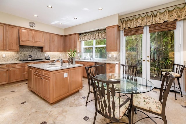 kitchen with a kitchen island with sink, light stone countertops, french doors, stainless steel dishwasher, and decorative backsplash