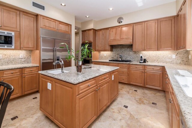 kitchen with tasteful backsplash, visible vents, built in appliances, a sink, and a kitchen island with sink