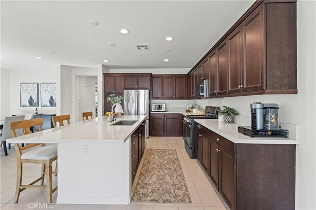 kitchen featuring visible vents, a breakfast bar, appliances with stainless steel finishes, light tile patterned flooring, and a sink