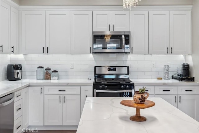kitchen featuring white cabinets, light stone countertops, backsplash, and appliances with stainless steel finishes