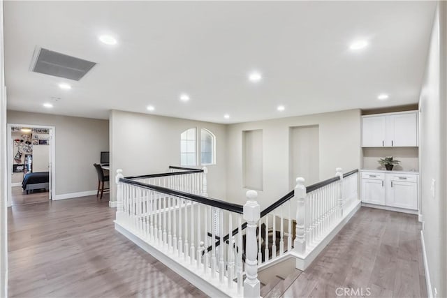 hall with light wood-style flooring, visible vents, an upstairs landing, and recessed lighting