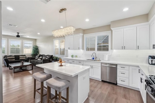 kitchen featuring visible vents, dishwasher, a sink, a kitchen breakfast bar, and range