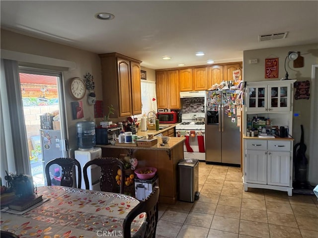 kitchen featuring light tile patterned floors, visible vents, gas range gas stove, stainless steel refrigerator with ice dispenser, and a healthy amount of sunlight