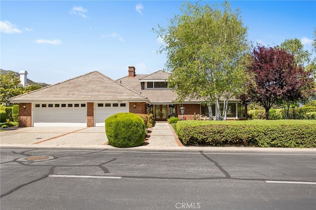 22316 Bear Creek Dr S, Murrieta, CA 92562 - view of front of home featuring brick siding, an attached garage, a chimney, and driveway