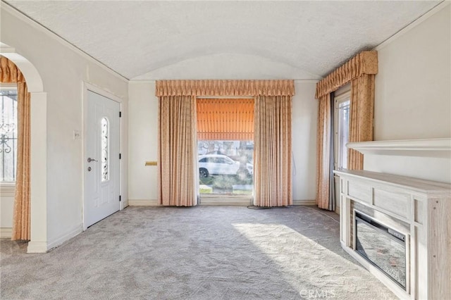 unfurnished living room with baseboards, arched walkways, carpet flooring, a glass covered fireplace, and lofted ceiling