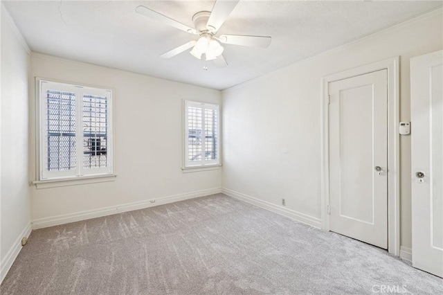 spare room featuring crown molding, baseboards, a ceiling fan, and carpet flooring