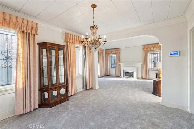 interior space with crown molding, an inviting chandelier, arched walkways, a glass covered fireplace, and carpet floors