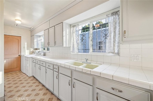 kitchen featuring tasteful backsplash, a sink, tile counters, and white cabinets